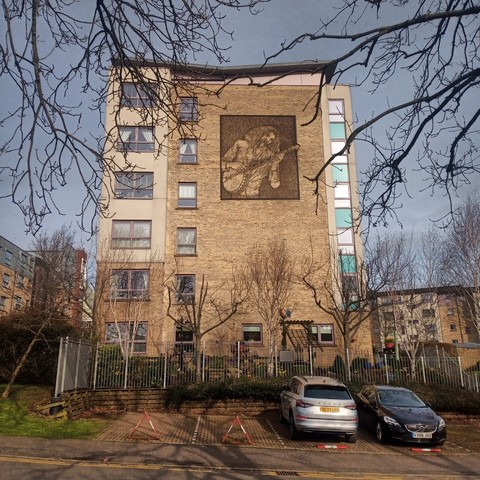 A block of flats in Glasgow with a metal artwork on the outside wall showing Billy Connolly playing a banjo.