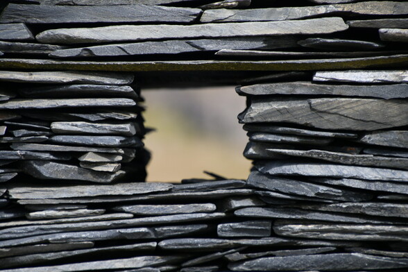 A window is seen in the centre of the photo, created by an artist who has made a stone sculpture on a beach of dark slate like layers of horizontal stone. This photo is a close up of the window. The landscape beyond the window is blurred.