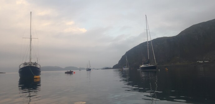 Halfway across Easdale Sound; boats sit quietly at their moorings on a calm sea. Dùn Mòr lurks in the background.