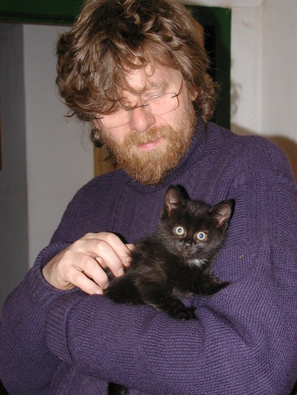 Penny, a very small black kitten, in my arms on the day she arrived with me in May 2006. She's staring at the camera with wide eyes. I have quite short hair and am wearing a blue fishermans jersey.