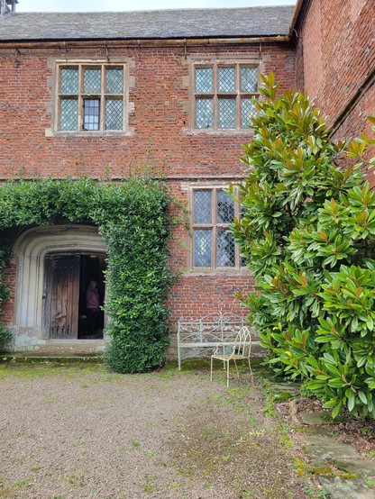 An external view of medieval Helens Manor showing a brick elevation with a tudor arched doorway and diamond-paned windows, remodelled in the C17th. The walls and doorways have creeper around them.