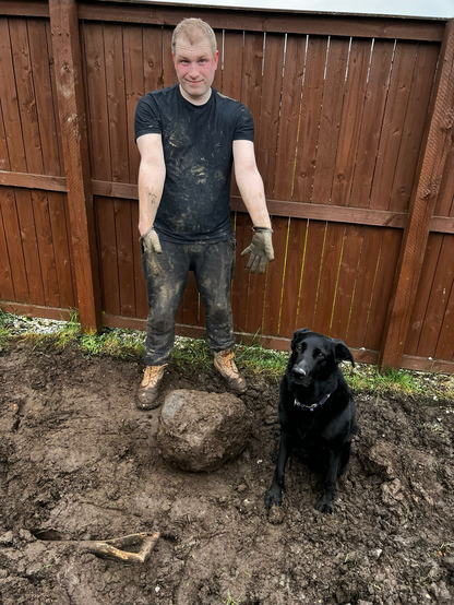 Man standing next to a dog and a rock the size of a small child