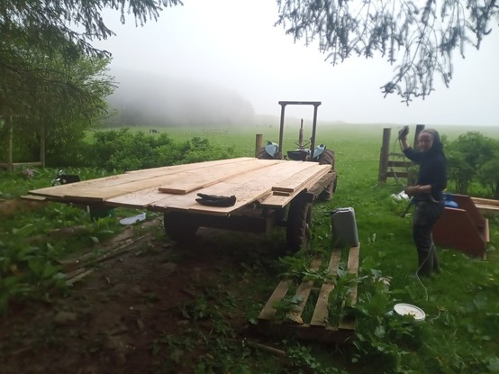 The Little Tractor That Can pointing up the hill into fog, with a trailer behind it entirely obscured by the pile of rough sawn boards it is carrying.