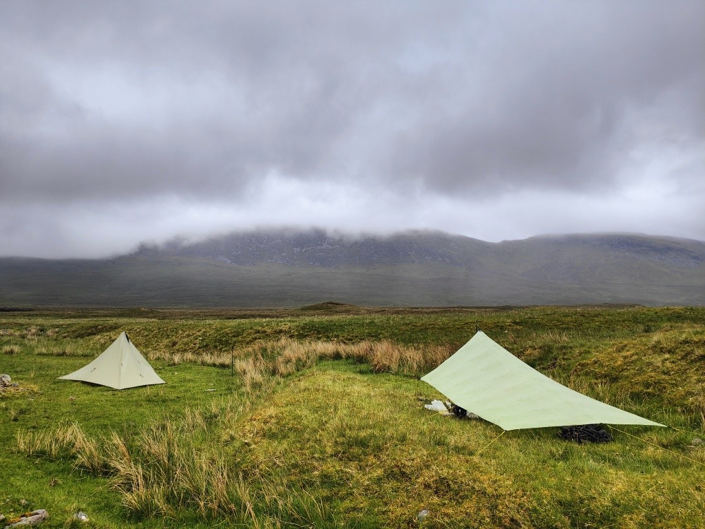 Two tents on rough ground with cloud-capped hills in the distance