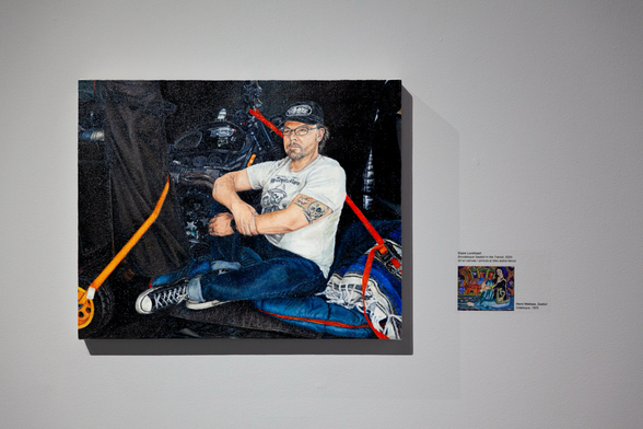 Brodalisque Seated in the Transit by Klaire Lockheart depicts a dude sitting on a sleeping bag in a van filled with motorcycle and other gear, which hangs on a gray gallery wall next to a museum label that includes a small print of Seated Odalisque by Henri Matisse.