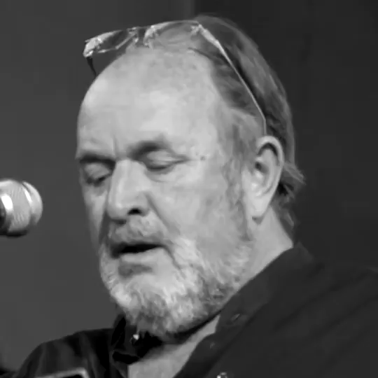 Black and white video of recent speech by historian Dalrymple. He is late middle-aged, receding hairline, smallish beard. He is wearing dark clothing and has his reading glasses pushed up on top of his head.