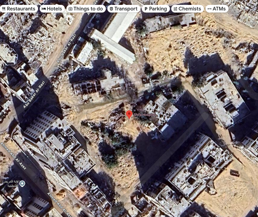 Google maps image of Shifa Hospital, near the port in Gaza city. It shows the hospital and most of the buildings around it reduced to rubble, with surviving buildings visibly damaged.